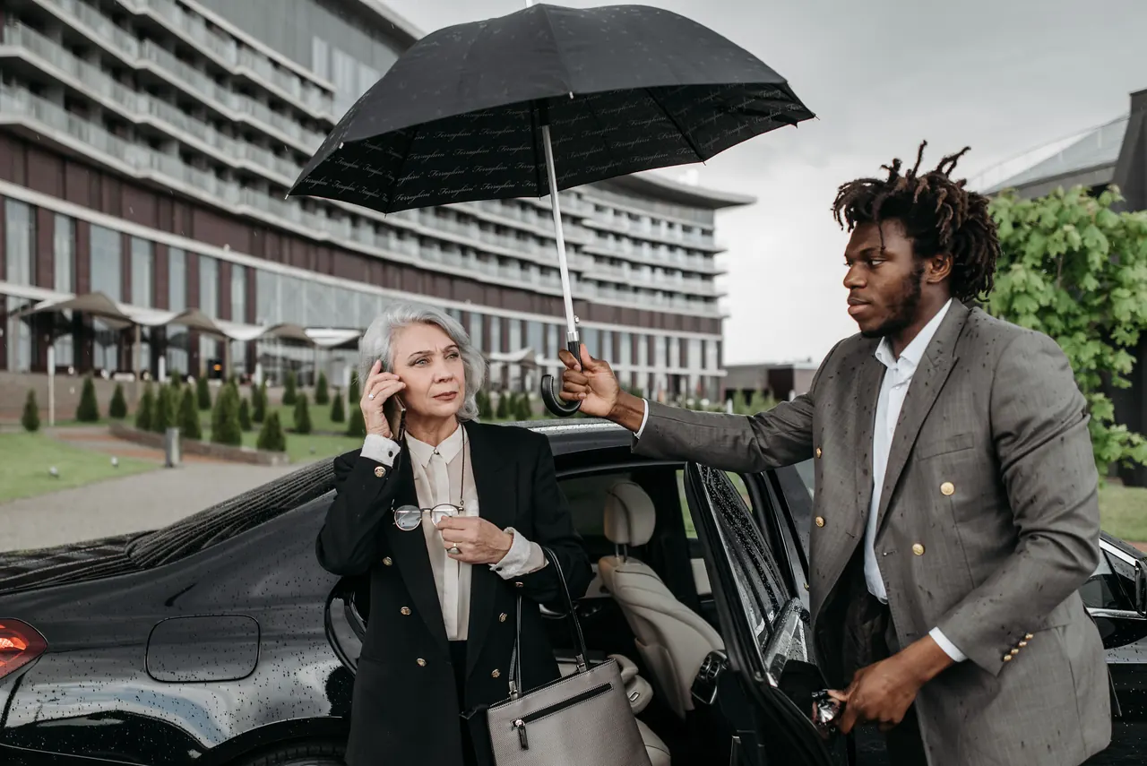 An AFSAHI chauffeur holding an umbrella for a client beside a black Mercedes