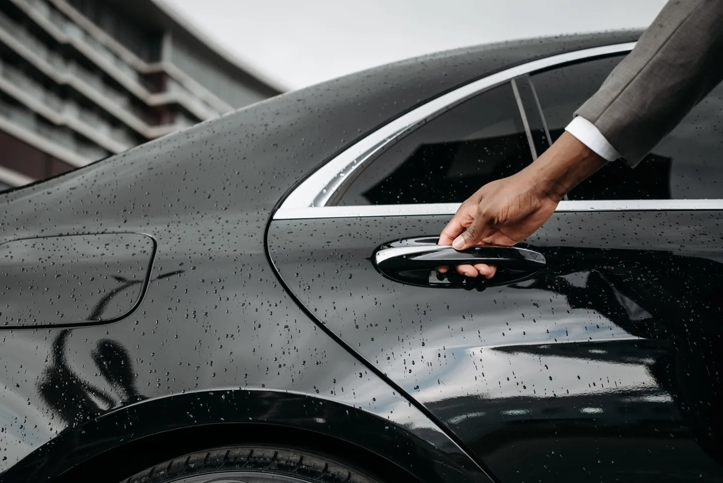 Chauffeur opening the rear door of a rain-flecked black luxury sedan
